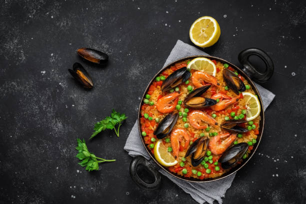 paella espanhola tradicional com frutos do mar em uma frigideira em um fundo de pedra preta. vista superior, plana. cozinha mediterrânea. - cozinha mediterrânica - fotografias e filmes do acervo