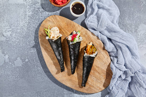 zestaw sushi temaki na drewnianym talerzu w minimalistycznym stylu. estetyczna kompozycja z ręcznymi rzeźmi na tle. współczesna kuchnia japońska - temaki sushi. - handroll zdjęcia i obrazy z banku zdjęć