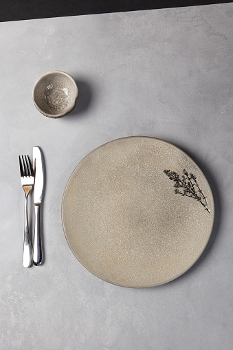 Ceramic dishware in modern style on gray stone background. Empty Handmade crockery with cutlery in minimalistic composition. Gray pottery plate on concrete background