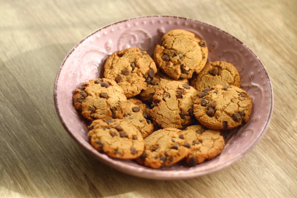 Tasty golden brown cardamom biscuits in small glass bowl on pink tablecloth.