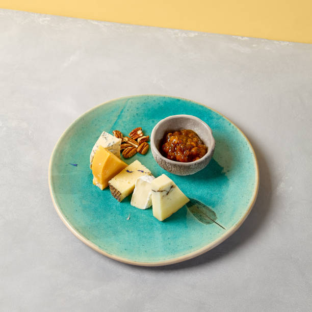 Cheese platter on blue ceramic plate. Cheeseboard on handmade dinner plate in modern style. Different cheese on ceramic dishware in minimal style