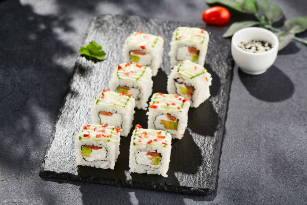 istock Fresh maki sushi on dark stone table. Colorful roll with vegetables. Sushi roll with salmon, avocado inside, cucumber outside. Style concept japanese menu with black background, leaves and hard shadow. 1392734962