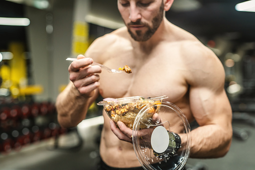 Powerful athletic man with great physique eating a healthy salad. Mockup your brand