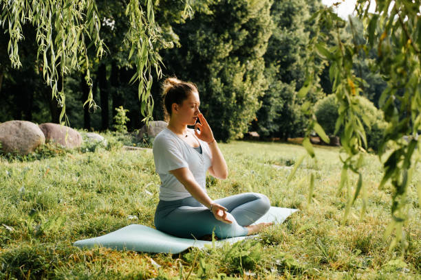 Side view of young woman practicing yoga asana breathing exercise sitting in lotus position with closed eyes on sports mat in nature. Yoga and meditation, healthy active lifestyle stock photo
