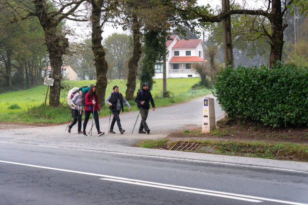 Arzua, Galicia, Spain. 05-15-2022. Several pilgrims walking with backpacks past one of the signs indicating the Camino de Santiago. stock photo