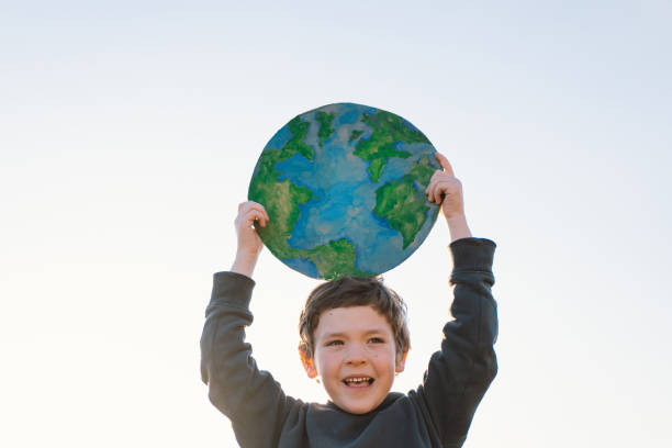 istock Little boy holding planet in hands against green spring background 1392737247