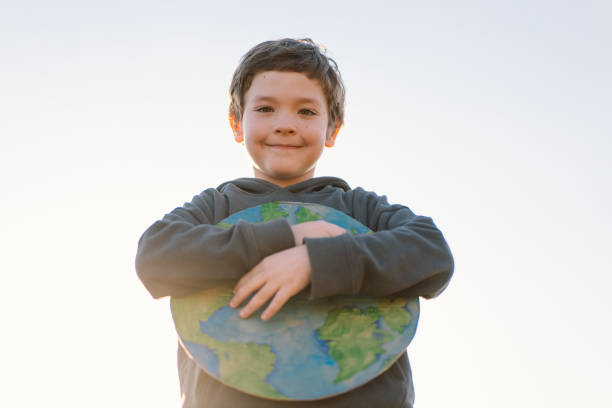 istock Little boy holding planet in hands against green spring background 1392737315