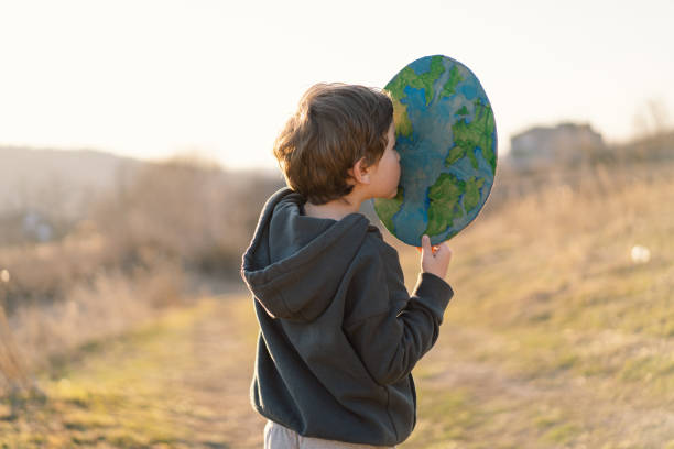 istock Little boy holding planet in hands against green spring background 1392737345