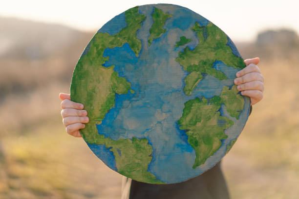 Protection and love of earth. Little boy holding planet in hands against green spring background. Earth day concept. Environmental Conservation