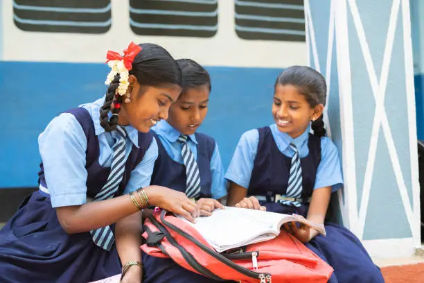 Photo of Group of girl kids studying from book at school corridor during break - concept of education, learning and knowledge.