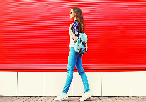 young woman full-length wearing backpack walking in the city on red background, blank copy space
