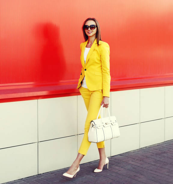 Beautiful young woman wearing yellow suit with handbag walking in the city on red background, street fashion stock photo