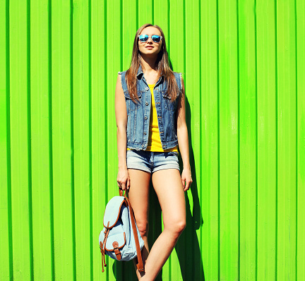 Summer portrait of beautiful young woman with backpack wearing sunglasses on green background