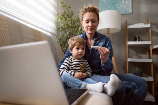 Caucasian mother with her toddler son having video call with pediatrician while holding thermometer stock photo