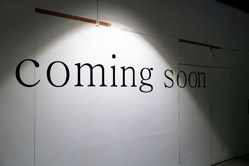 COMING SOON word on white background in the tungsten light on the wood cover fence or facade retail in under construction process.