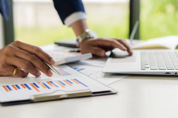 istock Businessman with pen pointing to graph, financial data, research, develop, market report. Strategic planning, analyzing, calculating financial accounts with calculator and laptop in the office. 1392753279