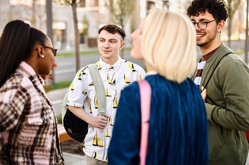 A multiethnic group of young people are walking on the sidewalk and chatting