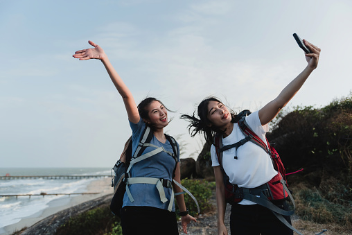 Two Asian female backpackers Taking a selfie using a smartphone with a smile