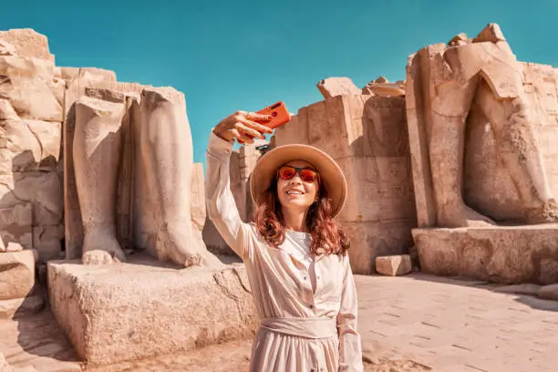 A blogger girl takes a selfie against the ruins of the grandiose Karnak temple in the ancient city of Luxor in Egypt