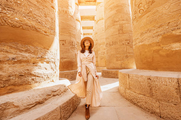 Happy woman traveler explores the ruins of the ancient Karnak temple in the heritage city of Luxor in Egypt. Giant row of columns with carved hieroglyph stock photo