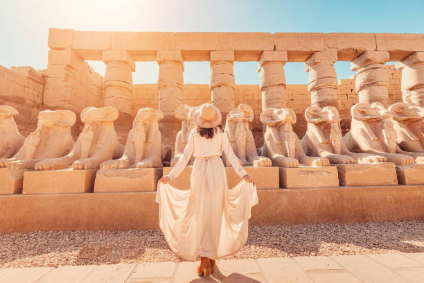 A happy tourist girl interested in Egyptology and archaeology and gets a travel experience at the Karnak Temple in Luxor among alley of sphinxes in Thebes stock photo