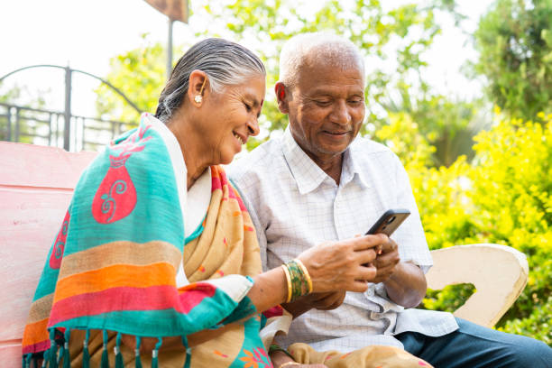 istock Senior couple using mobile phone while sitting on park - concept of social media, technology lifestyles and relaxation 1392761609