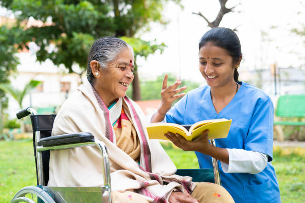 公園で本や小説を読んで笑う車椅子の看護師と年配の女性 - リラクゼーション、専門的な作業、治療または治療の概念 - senior adult doctor nurse senior women ストックフォトと画像