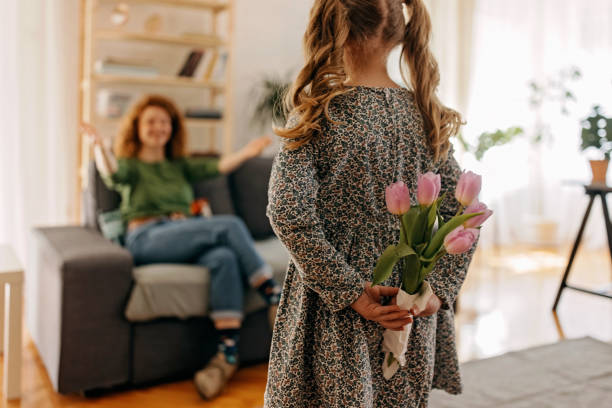 Daughter holding a bouquet of pink tulips behind her back is ready to give flower to her mother