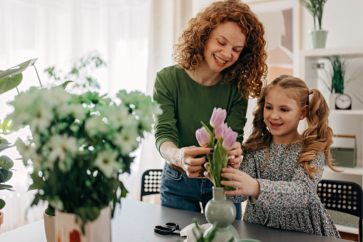 Cute girl helping mother to put tulips in the vase