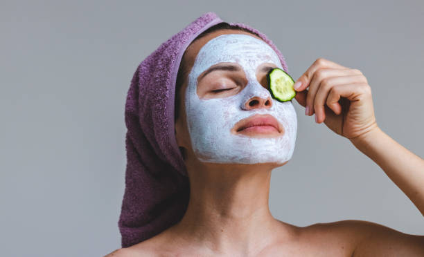 piękna młoda kobieta w ręczniku kąpielowym i w kosmetyce maska do pielęgnacji skóry nakładająca plasterek ogórka na oko. - cucumber human eye spa treatment health spa zdjęcia i obrazy z banku zdjęć