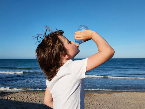 the child eagerly drinks water against the background of the sea, quenching his thirst in hot weather