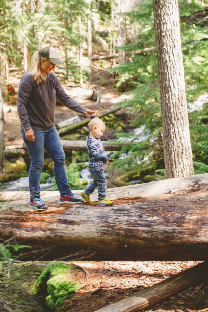istock Mother helps toddler walk along a log in forest 1392771149