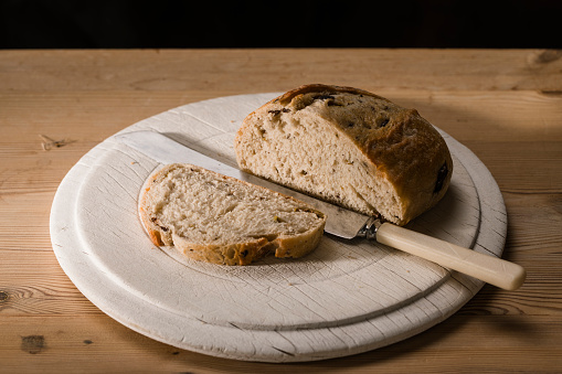 A close-up shot of a loaf of black olive and rye sourdough bread sliced on a cutting board on a wooden table.