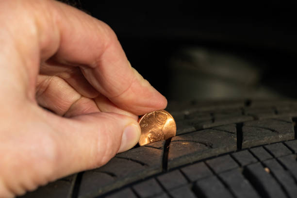 Checking tread depth on a tire by using a penny stock photo