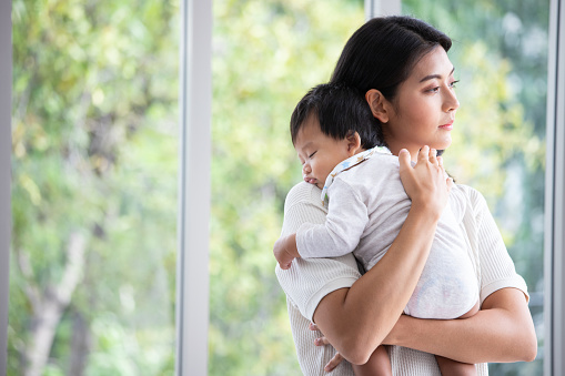 Mother embracing her baby girl while sleeping, lifestyle concept. Portrait of young woman and cute little baby in home interior. Motherhood concept