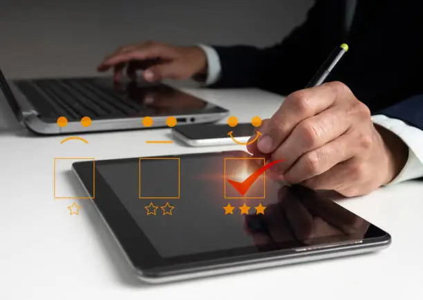 Photo of A man uses his laptop to select a facial smiling emoticon to display on the virtual screen. Survey, poll, questionnaire designed to gather information about user experience or customer satisfaction.