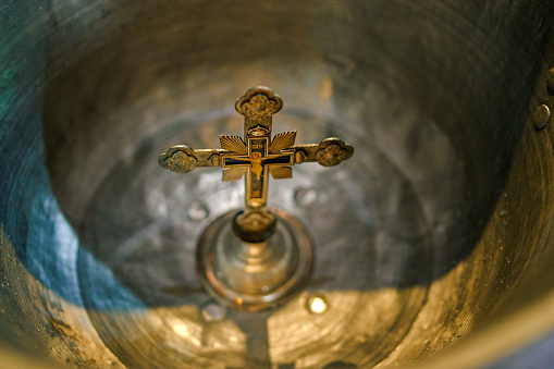 Aluminium church font, large bowl, with golden cross and saint water for the baptism of babies in Orthodox Church temple, Christening ceremony. Concept of rituals, sacraments of the Christian religion