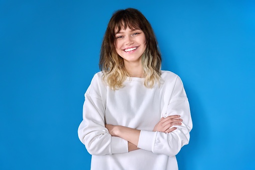 Portrait of teenage smiling female looking at camera on blue background. Positive confident successful young female student with arms crossed. Youth, beauty, success, education, confidence concept