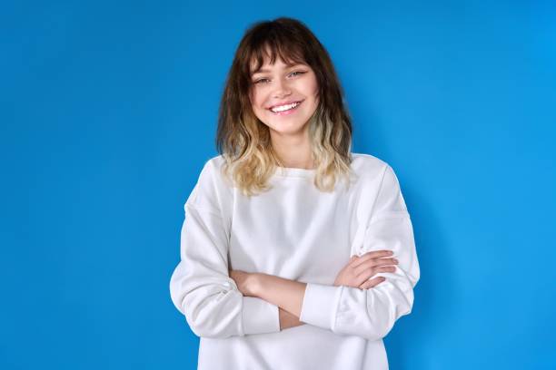 Portrait of a teenage smiling female looking at the camera on a blue background. Portrait of teenage smiling female looking at camera on blue background. Positive confident successful young female student with arms crossed. Youth, beauty, success, education, confidence concept young women stock pictures, royalty-free photos & images