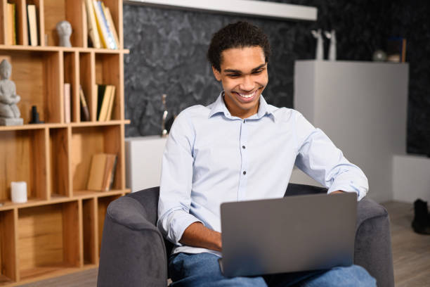 istock Young multiracial male student watching webinars, educational courses, learning on the distance. Front view of positive man in smart casual clothes using laptop while sitting 1392784550