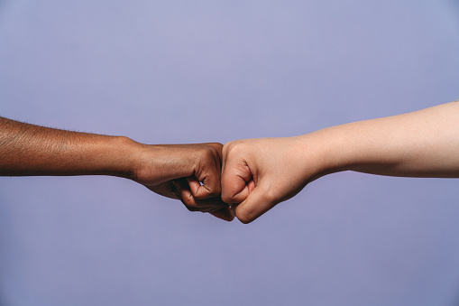 Two fists against a purple background. Conceptual shot about anti-racism and teamwork.