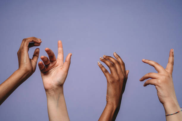 vier hände hoch vor einem violetten hintergrund - human hand reaching human arm gripping stock-fotos und bilder