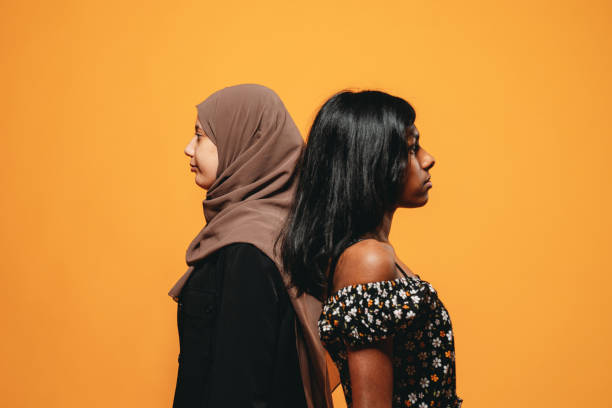 visão lateral de duas jovens mulheres adultas contra um fundo laranja - hijab profile teenager islam - fotografias e filmes do acervo