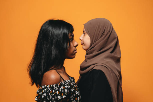 visão lateral de duas jovens mulheres adultas contra um fundo laranja - hijab profile teenager islam - fotografias e filmes do acervo