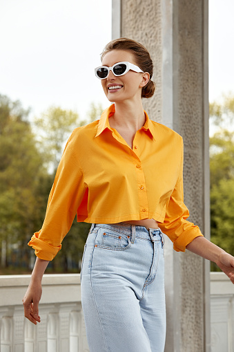 Outdoor fashion portrait of elegant, luxury woman wearing black sunglasses, trendy orange shirt and jeans. Copy, empty space for text.