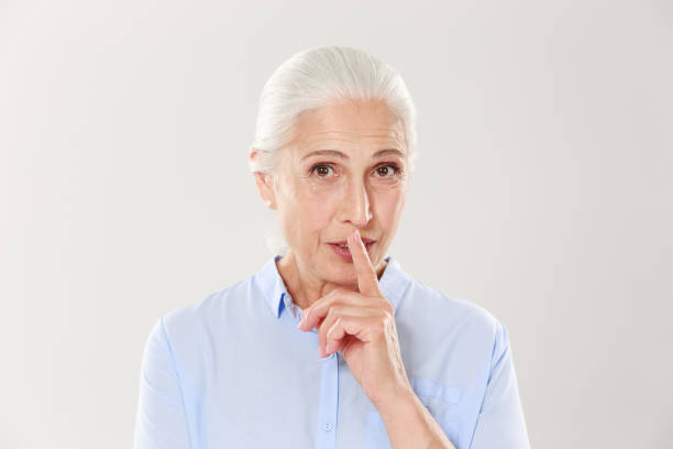 istock Beautiful old woman showing silence gesture, looking at camera 1392790466