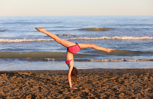 young athletic girl during a rhythmic gymnastics exercises with her legs up on the shore of the beach