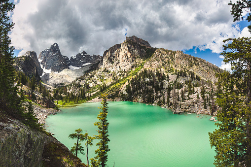 Teal green alpine lake, surrounded by mountains and stormy weather