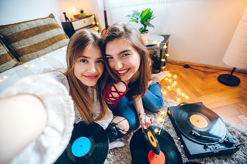 Two beautiful teenage sisters playing records and making selfies at home in lockdown.