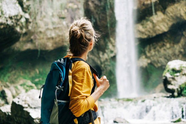 istock Young active unrecognizable woman from behind with a backpack looking at a waterfall in a canyon. 1392799407